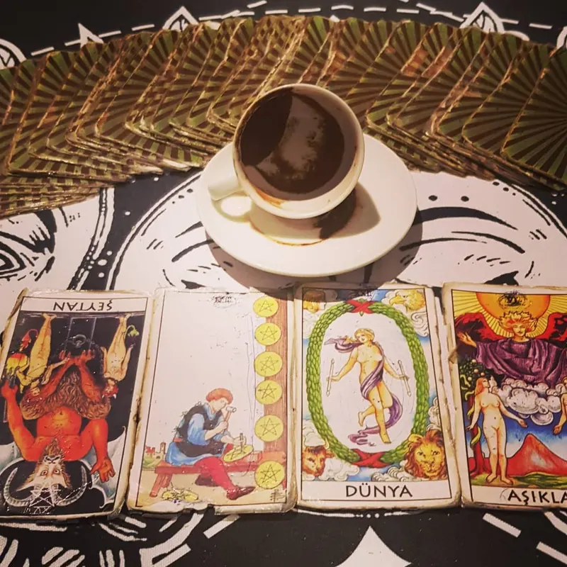 Güneş ve ay desenli örtüde üç açık tarot kartının üstünde, tabağına ters kapatılmış kahve fincanı