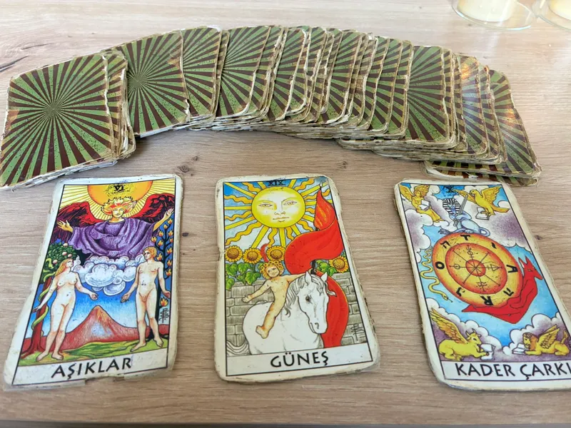Ahşap masada yelpaze gibi açılmış tarot destesi, önünde açık duran Aşıklar, Güneş ve Kader Çarkı kartları