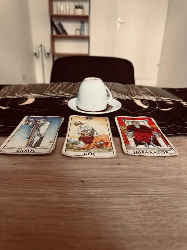 Ters kapatılmış kahve fincanı ve yelpaze gibi açılmış destenin önünde Ermiş, Güç ve İmparator tarot kartları